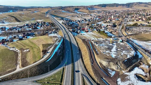 Viaduct over Klikuszowa village. New highway interchange on Zakopianka motorway with ramps, viaduct and traffic circle, joining the new highway with old road. Aerial revealing 4K video. January 2025