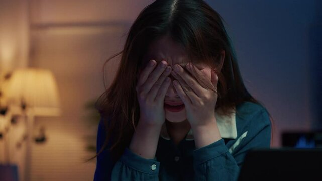 Sadness and desperation overwhelm a young businesswoman as she struggles with late-night work, expressing her frustration and emotional distress in the solitude of her home office