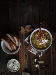 Vegetarian potato and bean soup served in rustic enameled bowl on wooden table. Sliced bread on the side
