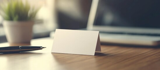 Blank business card on wooden desk with plant and laptop in background Copy Space
