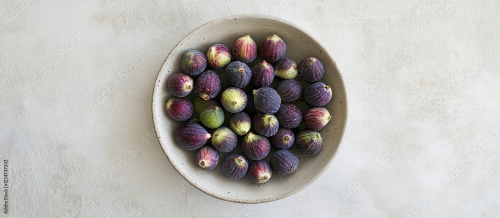 Poster bowl of fresh figs on a light textured surface with copy space for text placement