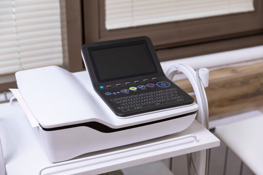 Electrocardiogram equipment for making cardiogram test of patient who is attached with vacuum sensors to the machine near coach in medical office room. Healthcare concept - Powered by Adobe