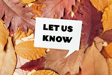White sign with the words let us know written on it is placed on top of a pi
