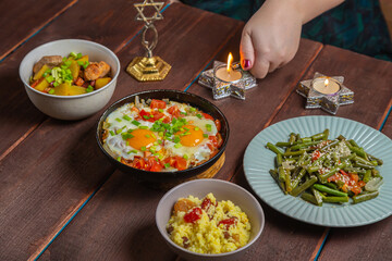 The hand of a Jewish woman lights Shabbat candles at a festive