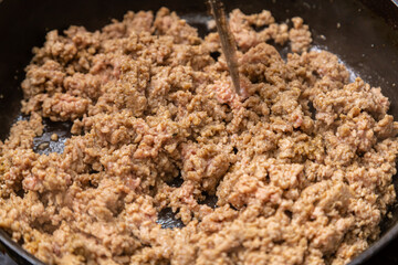 Frozen ground beef is fried with onions in a frying pan