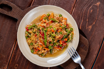 Couscous with vegetables in sauce in a plate on the table next to a fork