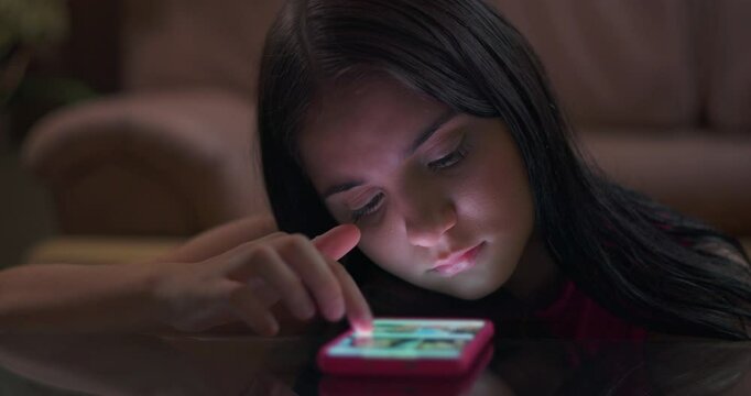 Teenager girl on table engrossed in phone with glowing light illuminating her face, illustrating youth caught in social media addiction and tech disconnection