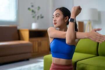 Asian woman is enjoying exercising and stretching her arms in her living room while wearing a smartwatch