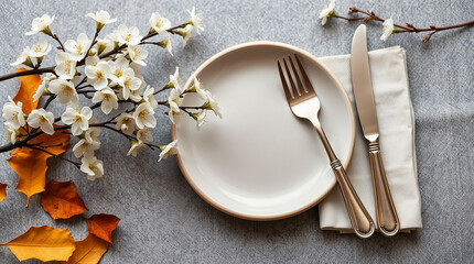 Empty plate with fork and knife near spring flowers and autumn leaves on gray background