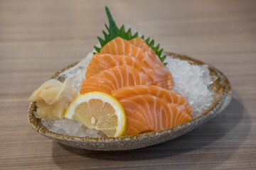 Salmon sashimi with vegetable, lemon and ice in a bowl, served in a restaurant