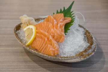 Salmon sashimi with vegetable, lemon and ice in a bowl, served in a restaurant