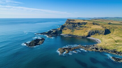 Aerial view of rugged coastal landscape with tranquil waters and green cliffs under a clear blue sky near a serene beach