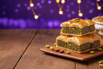 A plate of baklava with green pistachios and honey on a wooden table with purple background. Sweet dessert for Eid celebrations, Ramadan, Eid adha Mubarak or national holiday Iftar celebration.	

