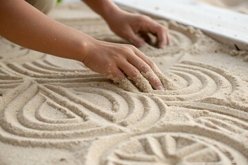 stress management, A person is creating intricate patterns in sand using their hands, showcasing artistry and creativity in a tranquil environment.