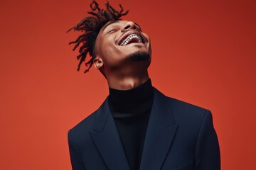 Fototapeta premium Smiling man with dreadlocks wearing a navy suit against a vibrant red background exuding confidence and joy