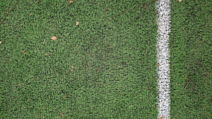 Outdoor artificial grass field on a children's playground. Artificial grass with white markings, top view. Football field, autumn. Old, worn and dirty artificial field for games © Mariia