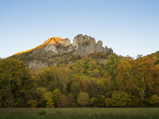 Seneca Rocks summit lit in the sunset with trees in fall colors in the foreground