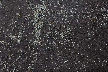 Small particles of anti-icing agent are scattered on the gray asphalt surface, providing traction and preventing ice formation in winter. Anti-icing agent on asphalt.