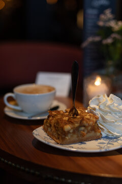 Piece of apple pie with whipped cream and a cup of cappuccino on a table in a restaurant 