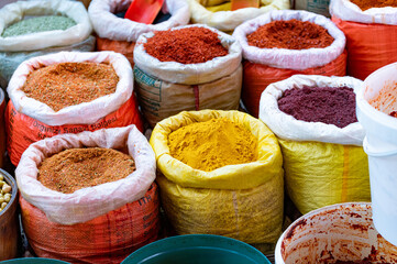 Colorful sacks filled with vibrant spices, including turmeric, chili, and other aromatic powders at a bustling market stall