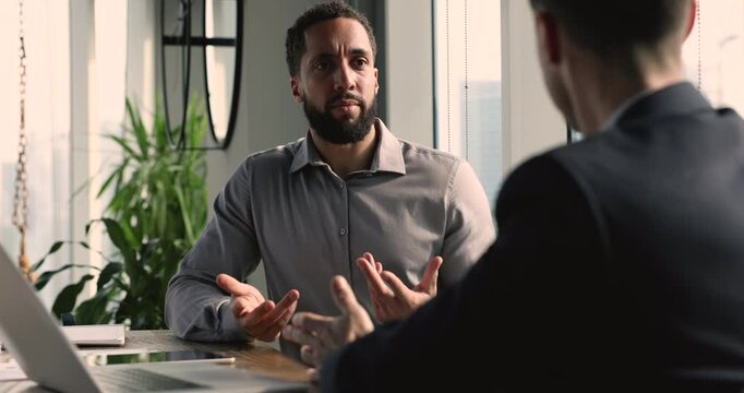 Serious African American entrepreneur consulting business expert, financial advisor, talking to co-worker, partner at workplace table. Businessman discussing project with partner