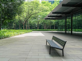 Obraz premium A modern, eco-friendly building with glass facades surrounded by lush greenery, featuring a sleek black bench on a spacious stone patio.