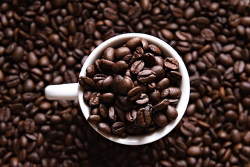 Roasted and brown decaf coffee beans inside a coffee cup. Top view. Roasted coffee beans on a surface. Coffee beans theme. 
