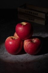 Close-up of a fresh red apple in dramatic moody lighting, placed on a dark stone surface with a rustic wooden crate in the background.
