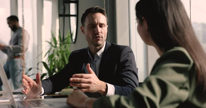 Latin businessman talking to female colleagues at workplace table in co-working space. Professional expert meeting with customer, giving consultation. Mentor training intern
