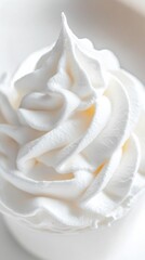 Close-up view of a swirl of white whipped cream with a smooth and fluffy texture, perfect as a background or culinary inspiration.