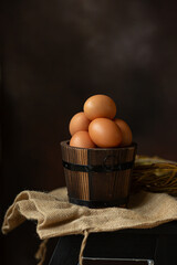 Brown chicken eggs in a small wooden bucket on dark background, for Easter