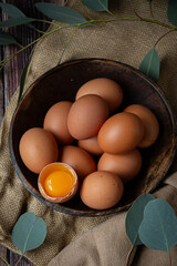 Brown chicken eggs in round wooden bowl, one egg is broken, perfect for Easter, natural light 