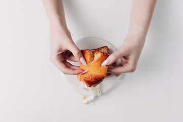 Woman's hands tearing, unwrapping, and crushing a pastry on a white plate against a white background