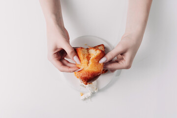 Woman's hands tearing, unwrapping, and crushing a pastry on a white plate against a white background