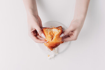 Woman's hands tearing, unwrapping, and crushing a pastry on a white plate against a white background