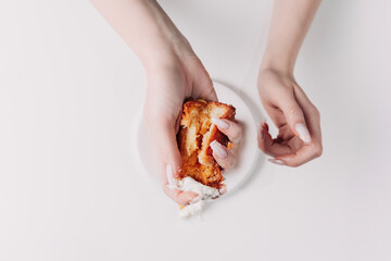 Woman's hands tearing, unwrapping, and crushing a pastry on a white plate against a white background