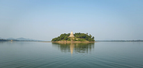 A serene view of Kalijai Island in Chilika Lake, Odisha. The island is home to a revered temple, surrounded by the calm, blue waters of the lake. The lush greenery of the island contrasts.
