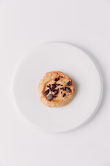 Round cookie with chocolate crumbs on a white plate against a white background