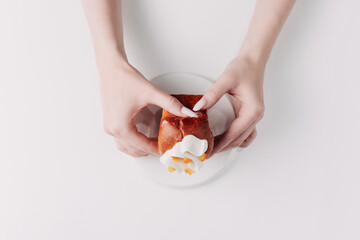 Woman's hands tearing, unwrapping, and crushing a pastry on a white plate against a white background