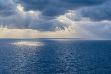 Obraz premium Sunbeams through the clouds illuminating the sea.