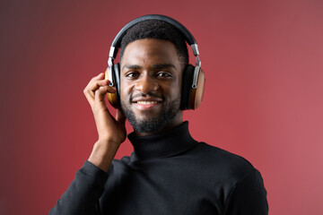 Smiling young African man wearing headphones against a vibrant red background, showcasing joy and...