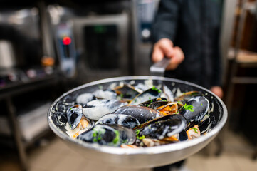 A chef presents a skillet of freshly cooked mussels garnished with herbs, showcasing vibrant seafood in a professional kitchen setting. Perfect for culinary themes and seafood recipes.