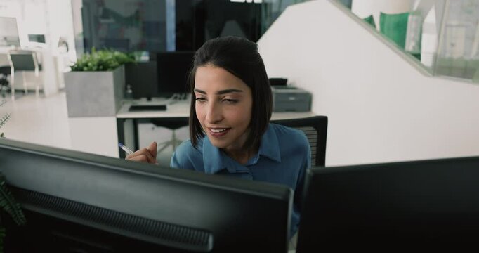 Latin woman using dual monitors, performing tasks that require multitasking, comparing spreadsheets or charts across two screens, working on graphic design, video editing, tracking real-time updates