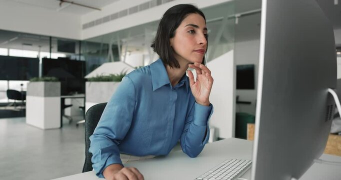 Focused Latina woman working on PC computer in contemporary coworking space, engaged in professional or analytical tasks completion, reviewing reports or financial data, drafting or editing documents