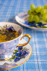 The image depicts an elegant tea cup alongside a plate of grapes on a blue checked tablecloth, displaying a delightful and inviting dining experience.