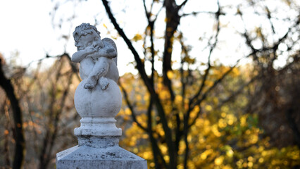 angel statue in the park. little boy with wings. cupid statue in autumn park. figurine for design, marble sad angel sitting on a ball. blurred natural background. 