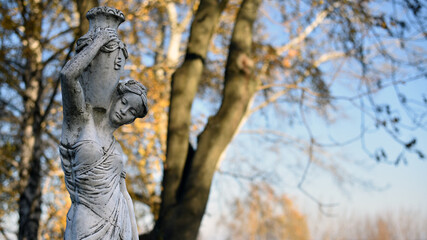 sculpture of a girl in the autumn park. An old statue in a park of a sensual semi-nude Greek or Italian Renaissance woman with a vase. sunny day, spring garden. 
