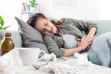 Young woman lying on the couch, holding her stomach in pain, suffering from abdominal discomfort...