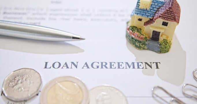 Loans, financial agreements, mortgages, real estate, and home ownership. A loan agreement document with a small model house, a ballpoint pen, coins, symbolizing the financial agreement and planning.
