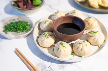 A close-up of steamed dumplings topped with chopped green onions and paired with soy sauce.